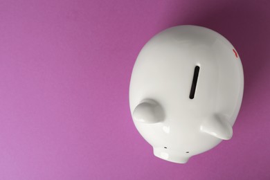 Photo of Ceramic piggy bank on purple background, top view. Space for text