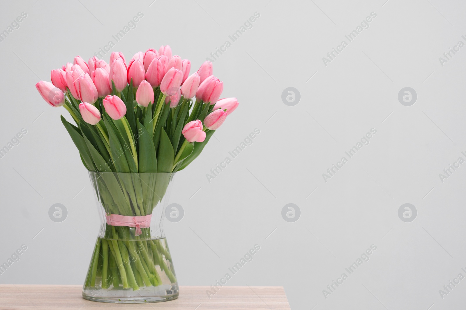 Photo of Bouquet of beautiful pink tulips in vase on wooden table against grey background, space for text