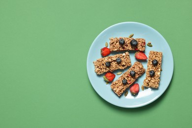 Tasty granola bars and berries on green background, top view. Space for text