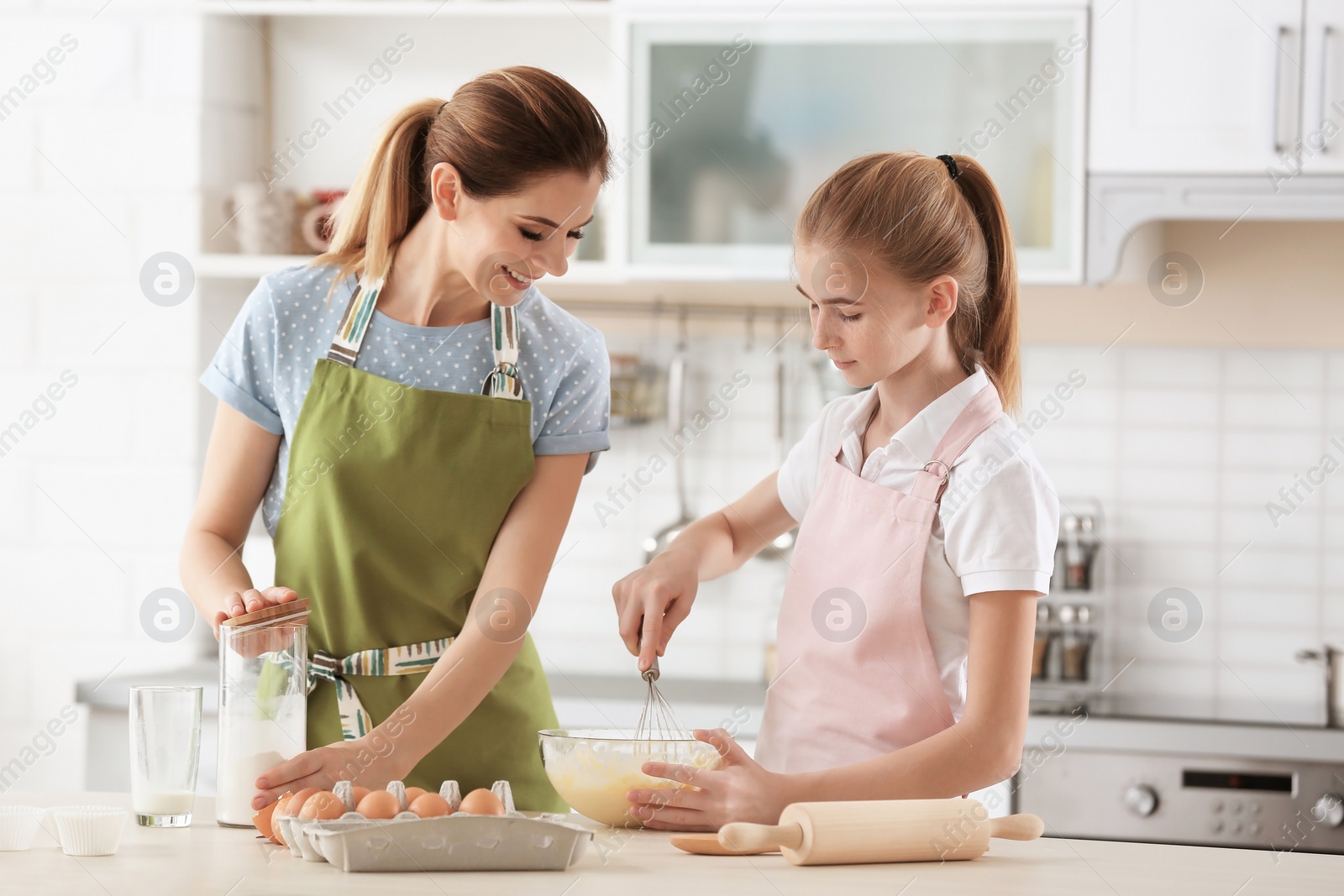 Photo of Mother and her daughter making dough at table in kitchen