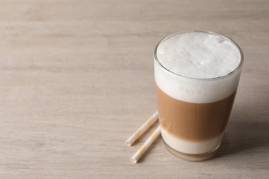 Photo of Glass of delicious layered coffee and straws on wooden table, space for text