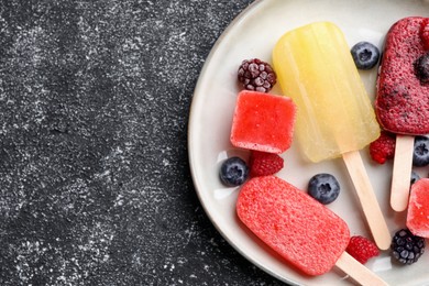 Photo of Plate of different fruit ice pops on black textured table, top view. Space for text