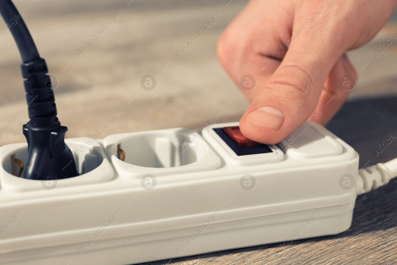 Photo of Man pressing power button of extension board on floor, closeup