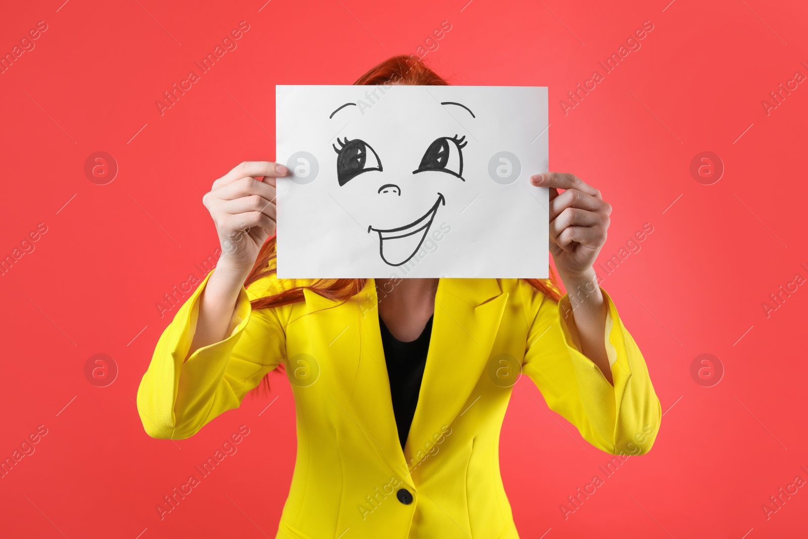 Photo of Woman hiding behind sheet of paper with happy face on red background