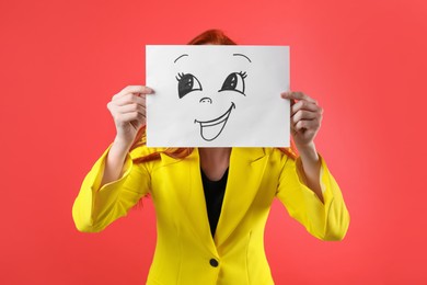 Woman hiding behind sheet of paper with happy face on red background