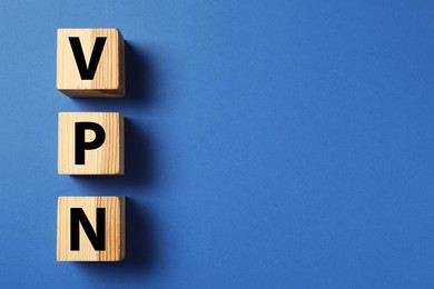 Wooden cubes with acronym VPN on blue background, flat lay. Space for text