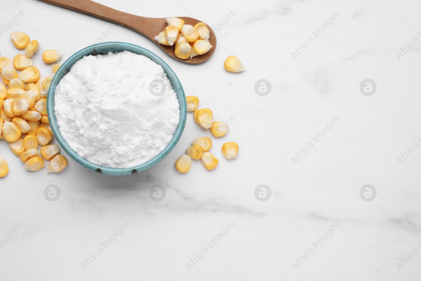 Photo of Bowl with corn starch and kernels on white marble table, flat lay. Space for text