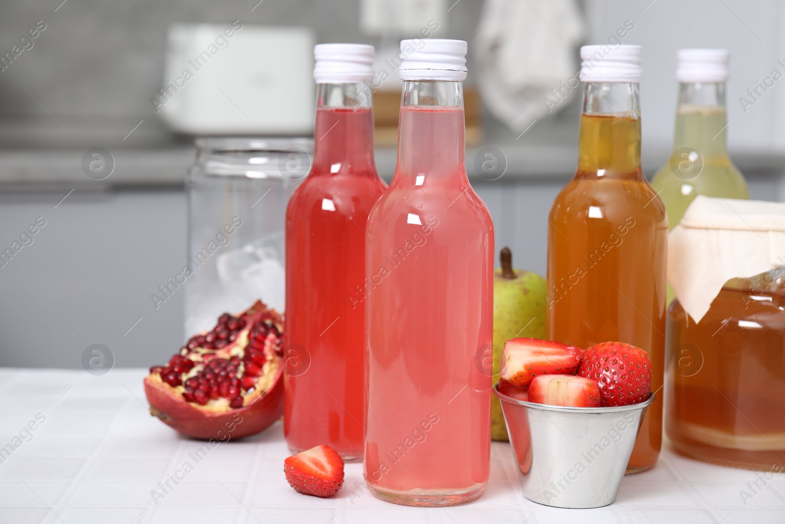 Photo of Tasty kombucha in glass bottles, jar and fresh fruits on white tiled table