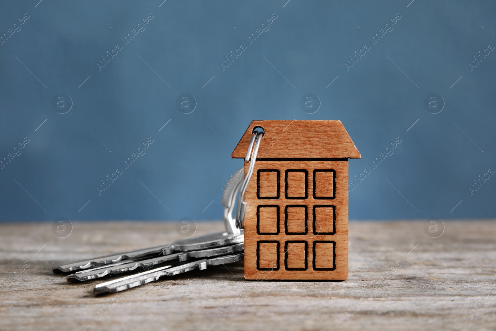 Photo of House keys with trinket on wooden table against color background. Space for text