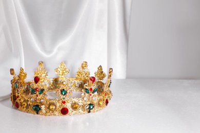 Beautiful golden crown with gems on light grey table. Space for text