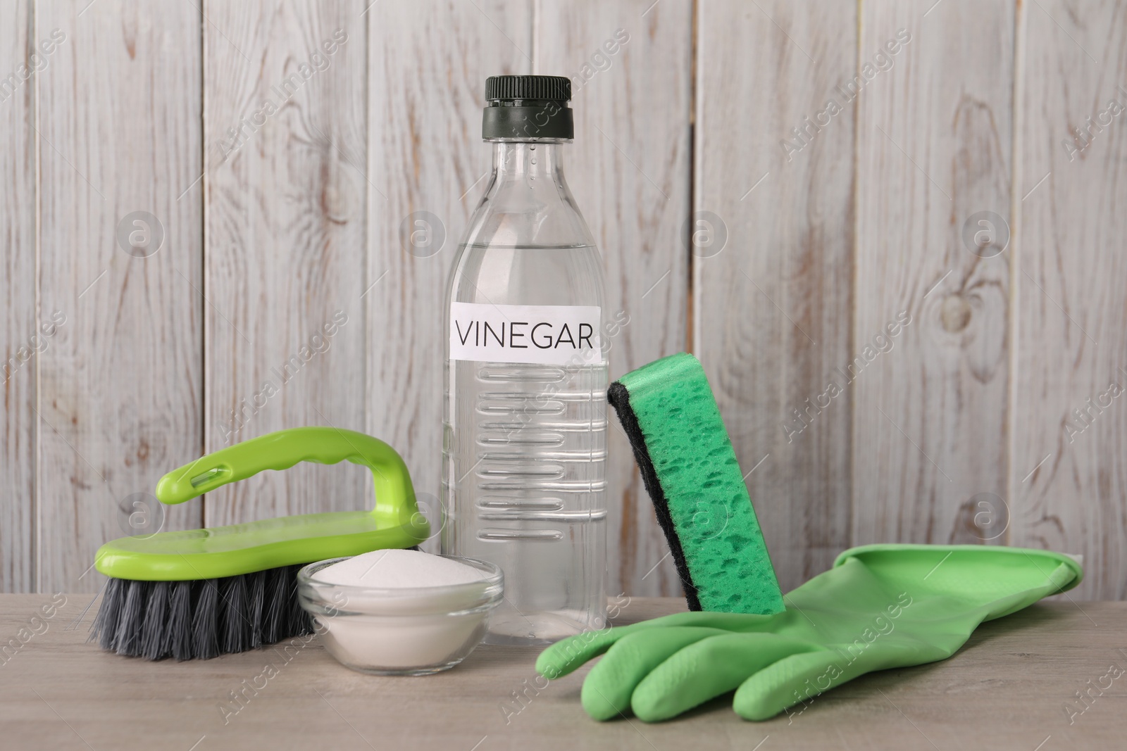 Photo of Natural cleaning products. Vinegar in bottle, baking soda, glove, sponge and brush on light wooden table