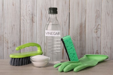 Natural cleaning products. Vinegar in bottle, baking soda, glove, sponge and brush on light wooden table