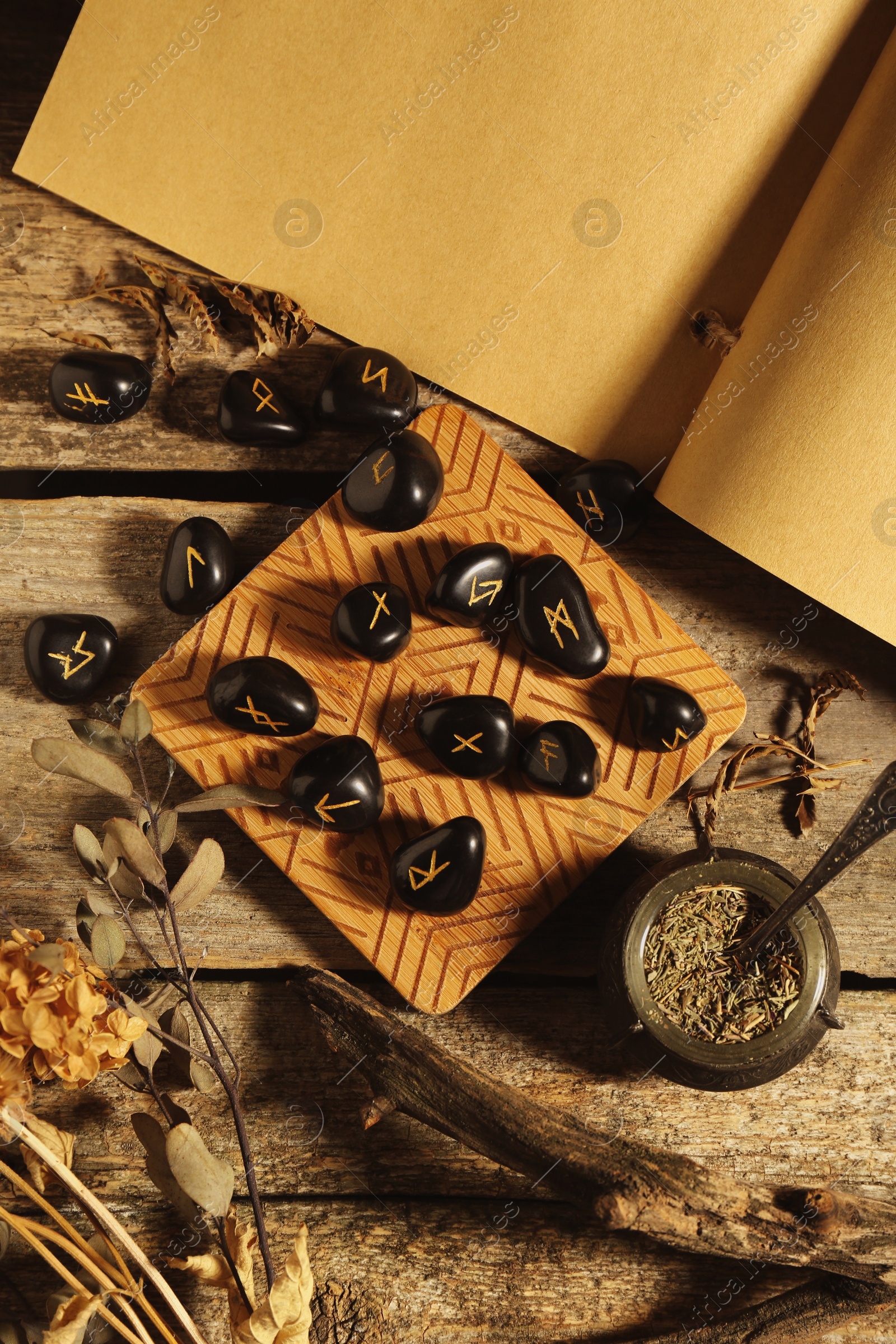 Photo of Many black rune stones, old book and dried plants on wooden table, flat lay