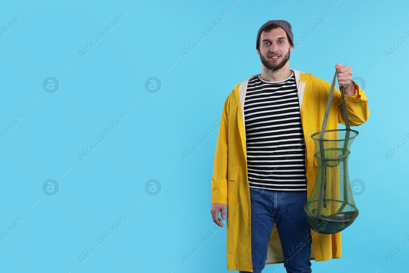 Photo of Fisherman holding fishing net with catch on light blue background, space for text