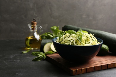 Photo of Delicious zucchini pasta with basil in bowl on black slate table. Space for text