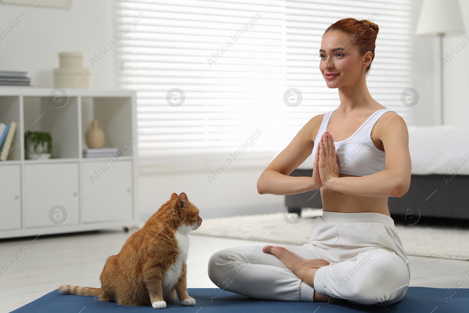 Photo of Beautiful woman with cute red cat practicing yoga on mat at home