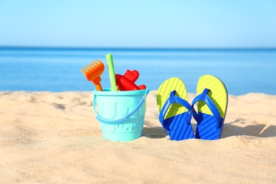 Photo of Beautiful view of sand with plastic beach toys and flip flops near sea on sunny day