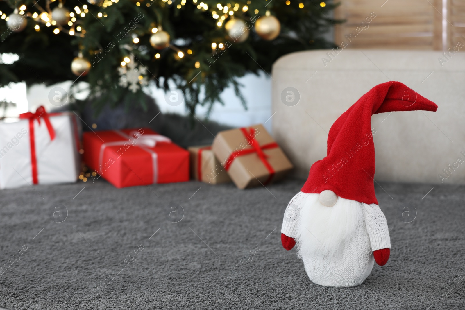 Photo of Cute Scandinavian gnome on carpet near Christmas tree and gift boxes in room. Space for text