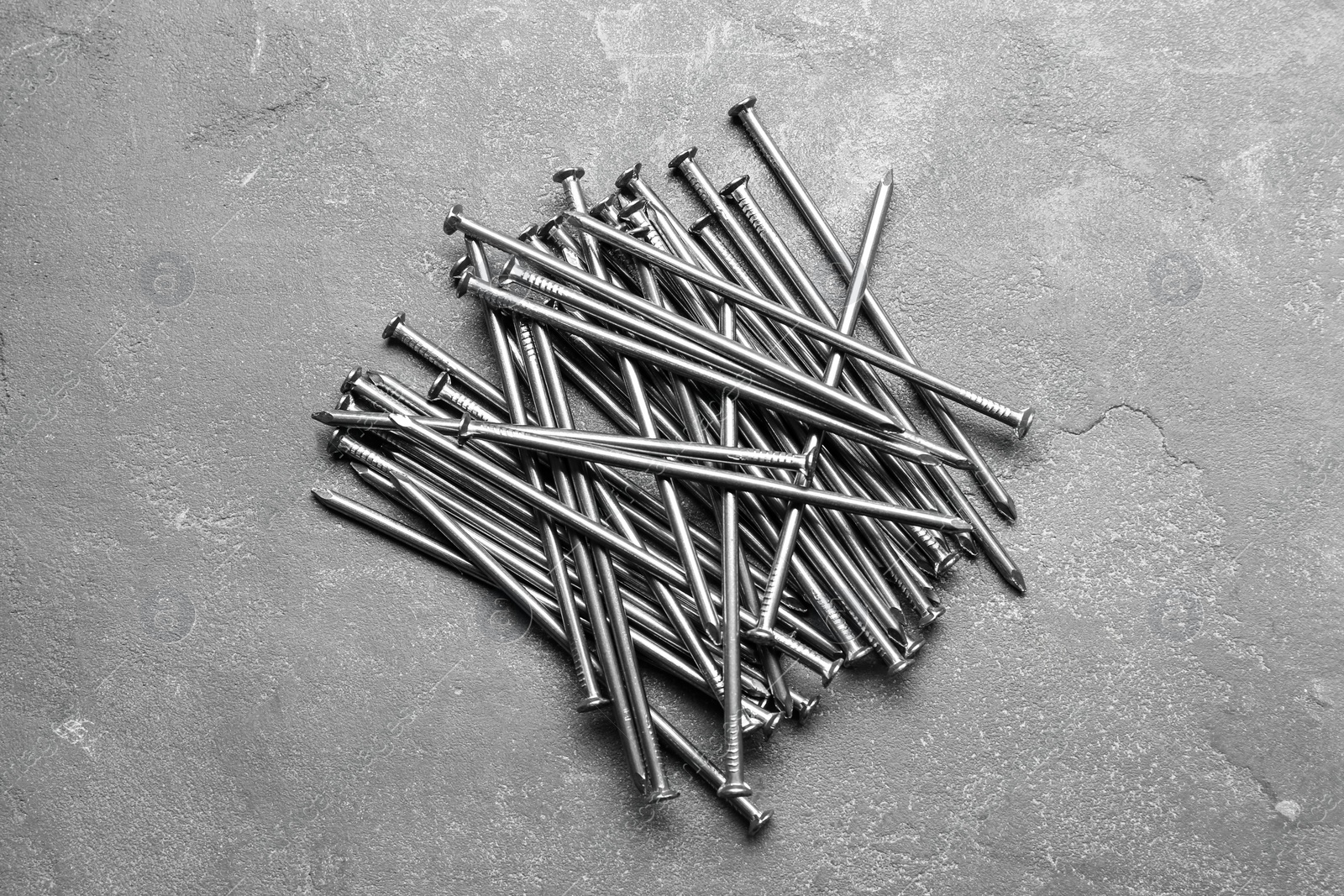 Photo of Pile of metal nails on grey stone background, flat lay