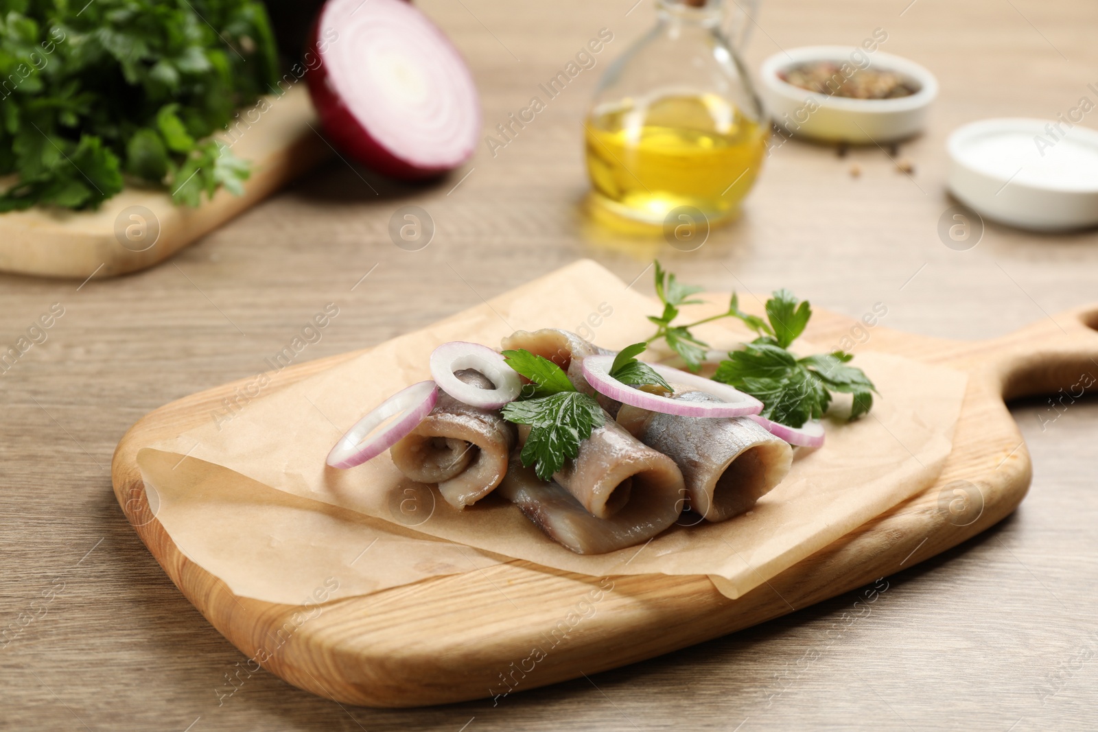 Photo of Board with delicious salted herring fillets, onion rings and parsley on wooden table