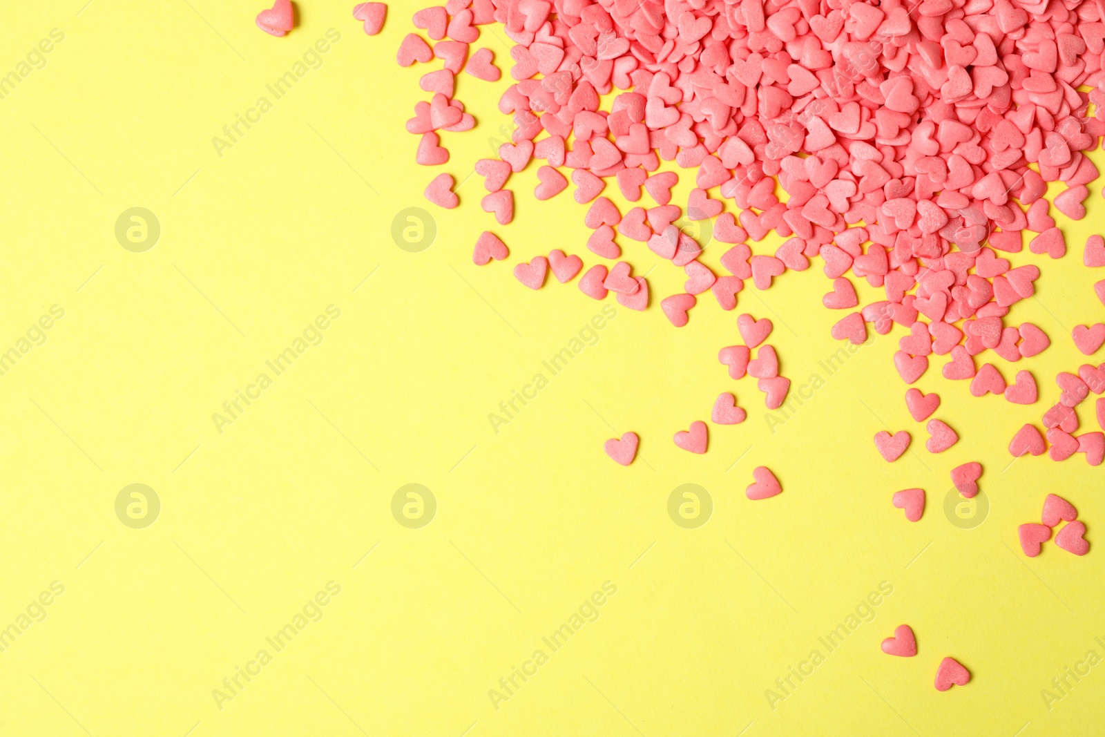 Photo of Bright heart shaped sprinkles on yellow background, flat lay. Space for text