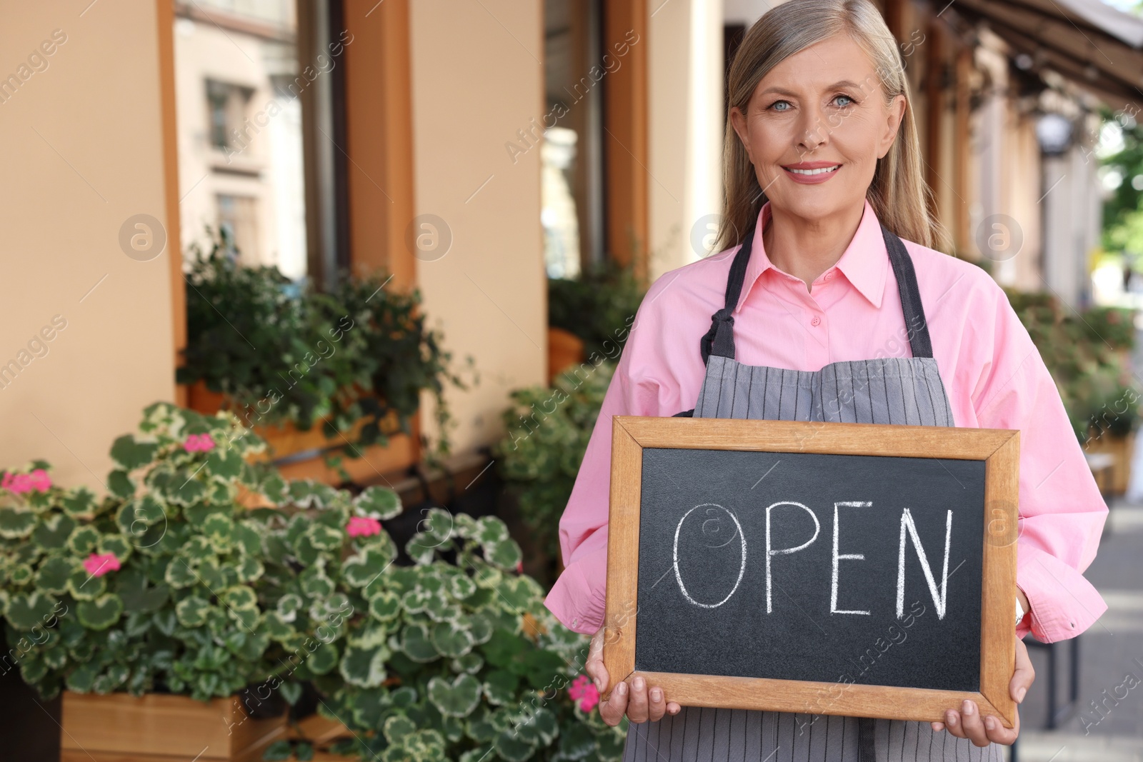 Photo of Happy business owner holding open sign near her cafe outdoors, space for text