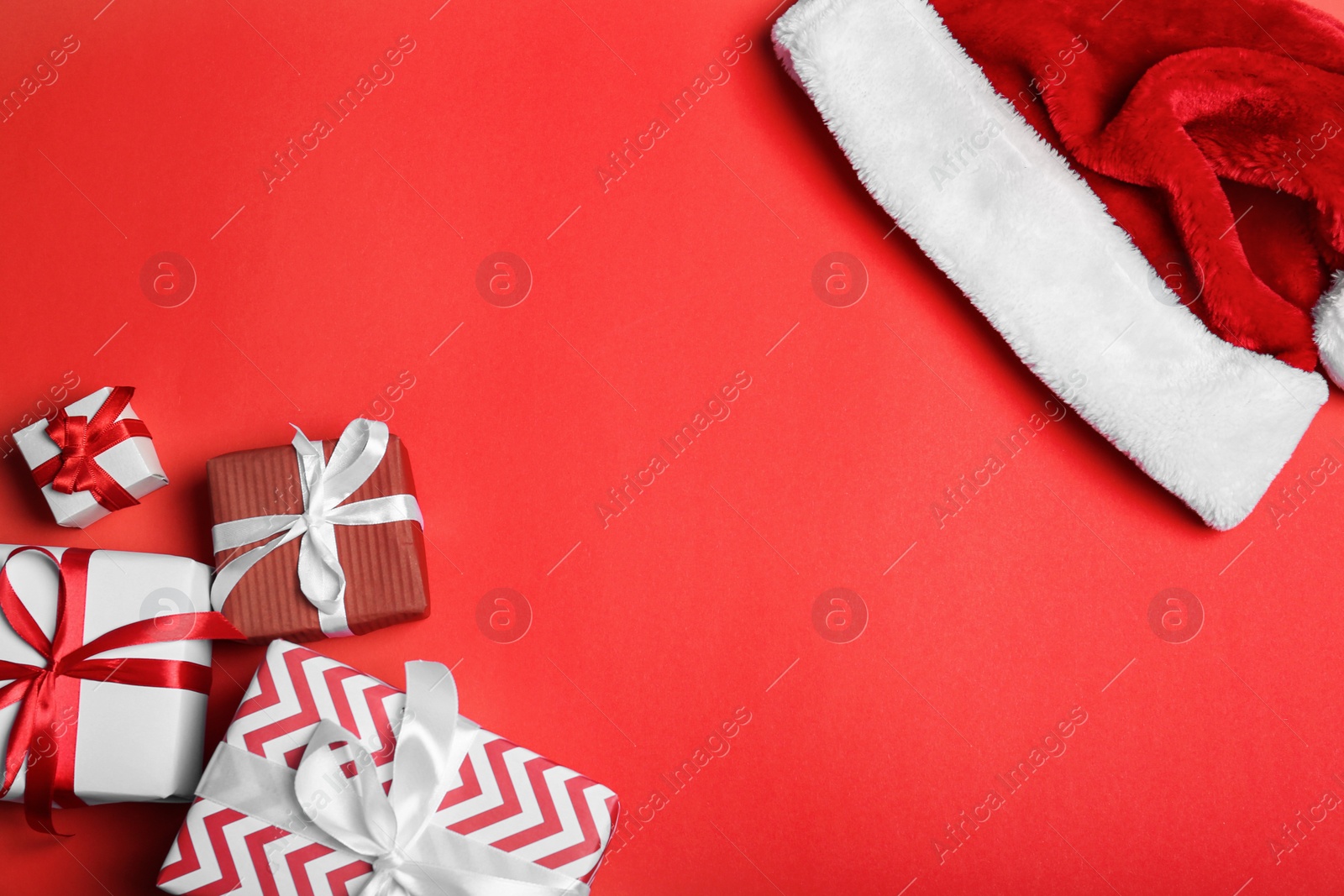 Photo of Santa Claus red hat and gift boxes on color background, top view