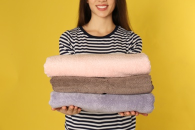 Photo of Young woman holding clean laundry on color background, closeup