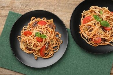 Photo of Delicious pasta with anchovies, tomatoes and olives on wooden table, flat lay