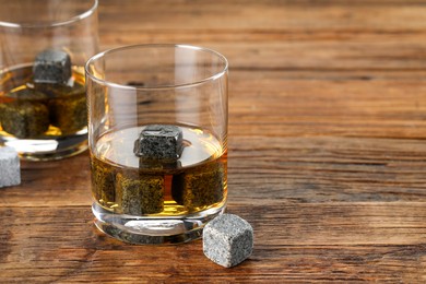 Whiskey stones and drink in glasses on wooden table, closeup. Space for text