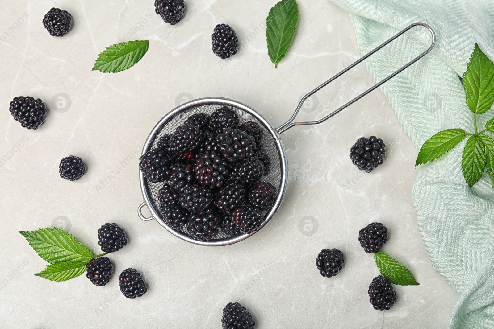 Photo of Flat lay composition with strainer of fresh blackberry and leaves on gray background