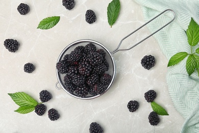 Photo of Flat lay composition with strainer of fresh blackberry and leaves on gray background