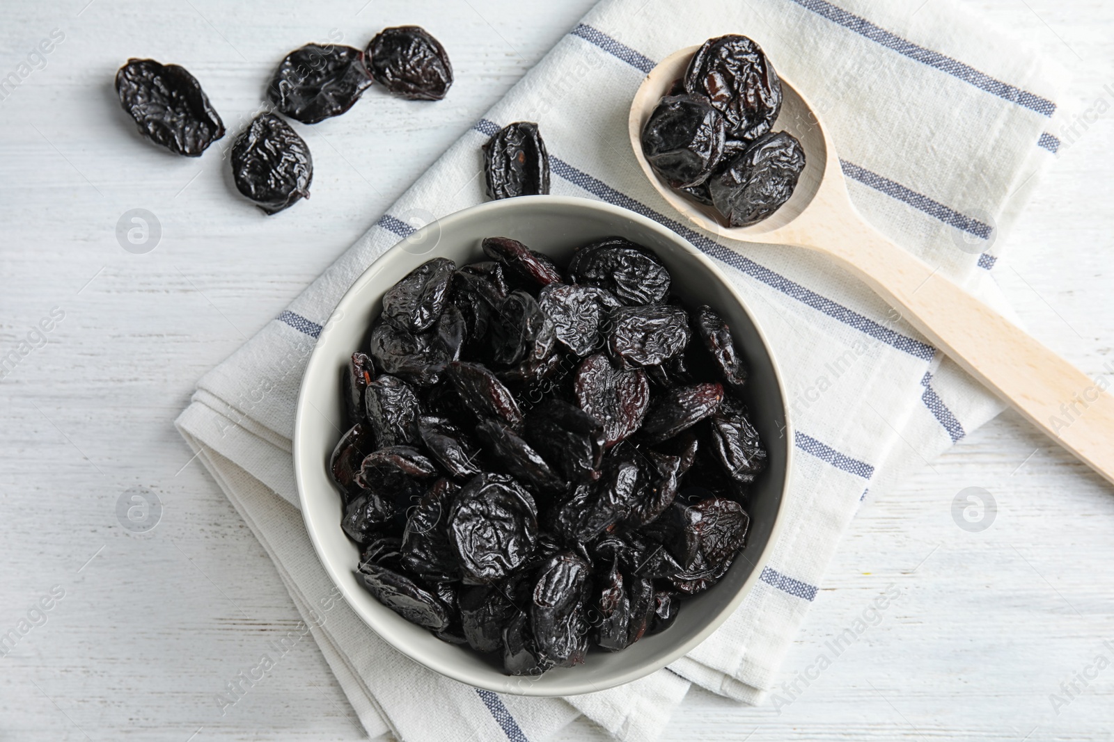 Photo of Bowl and spoon of sweet dried plums on table, top view. Healthy fruit