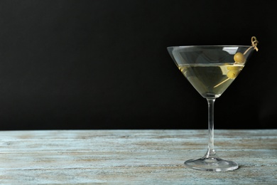 Photo of Glass of Classic Dry Martini with olives on wooden table against black background. Space for text