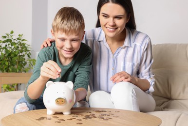 Photo of Boy with his mother putting coin into piggy bank at home