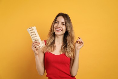 Young woman with delicious shawarma on yellow background