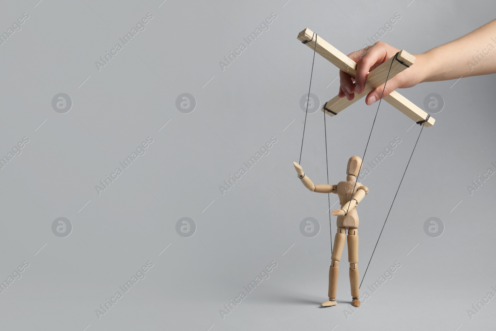 Photo of Woman pulling strings of puppet on light grey background, closeup. Space for text