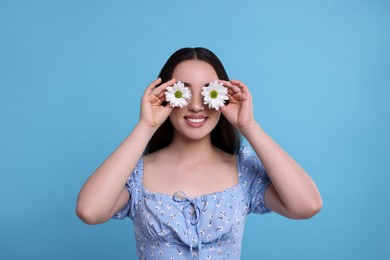 Photo of Woman covering her eyes with spring flowers on light blue background