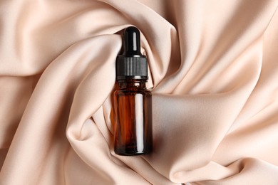 Photo of Bottle of organic cosmetic product on beige silky fabric, top view