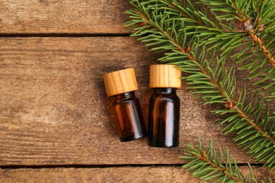 Photo of Bottles of pine essential oil and conifer tree branches on wooden table, flat lay. Space for text