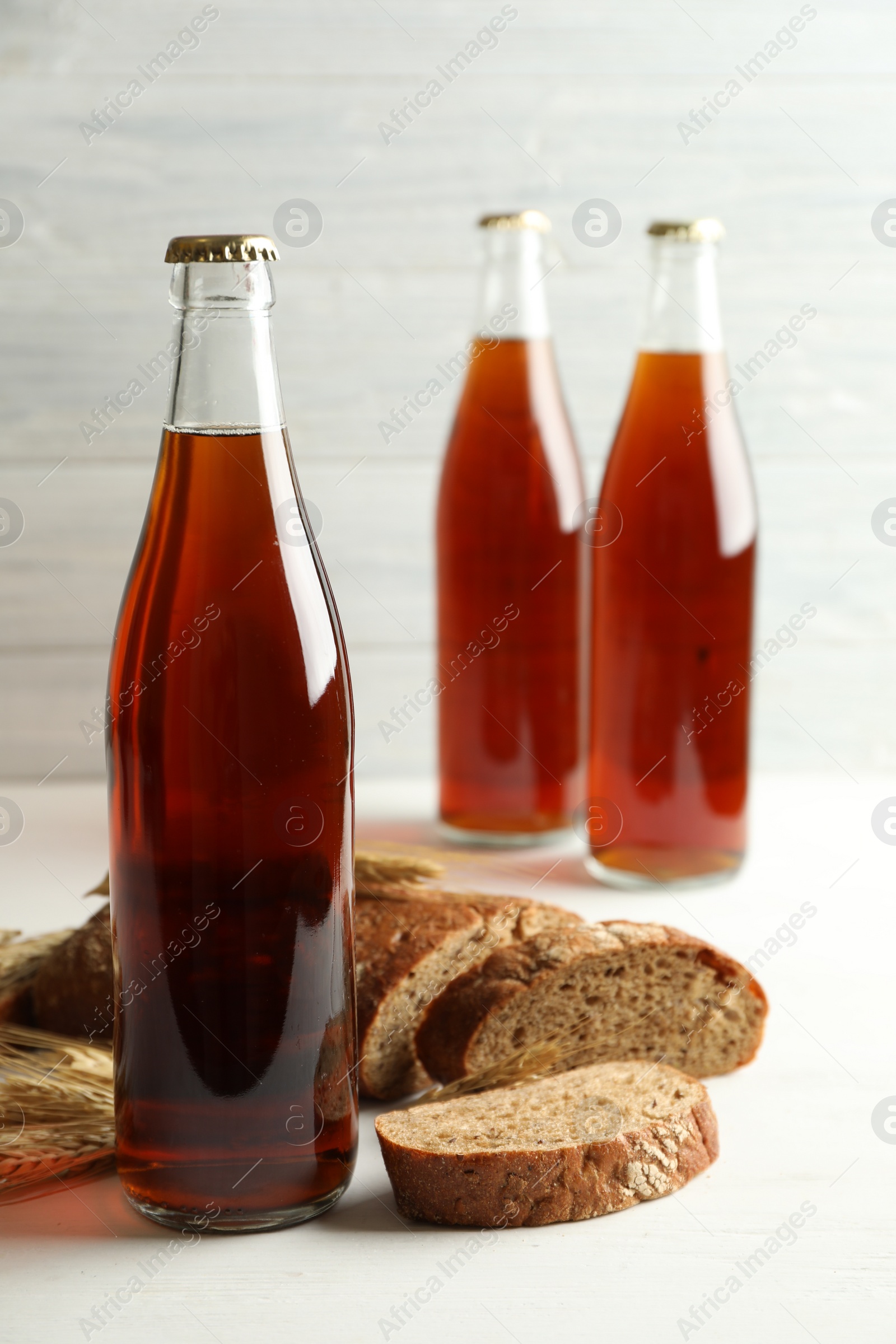 Photo of Bottle of delicious fresh kvass, spikelets and bread on white wooden table