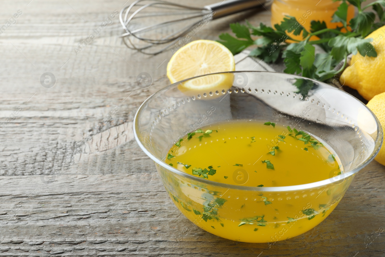 Photo of Bowl with lemon sauce and ingredients on wooden table, space for text. Delicious salad dressing