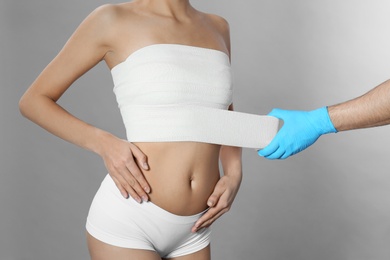 Photo of Doctor bandaging young woman after plastic surgery operation on grey background, closeup