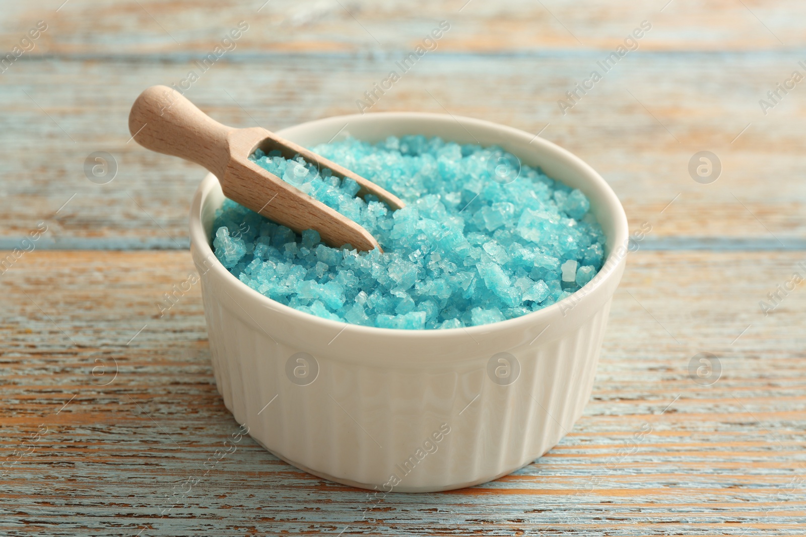 Photo of Bowl and scoop with turquoise sea salt on rustic table, closeup