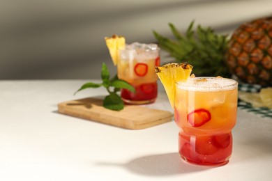 Photo of Spicy pineapple cocktail with chili pepper and ice cubes on white table. Space for text