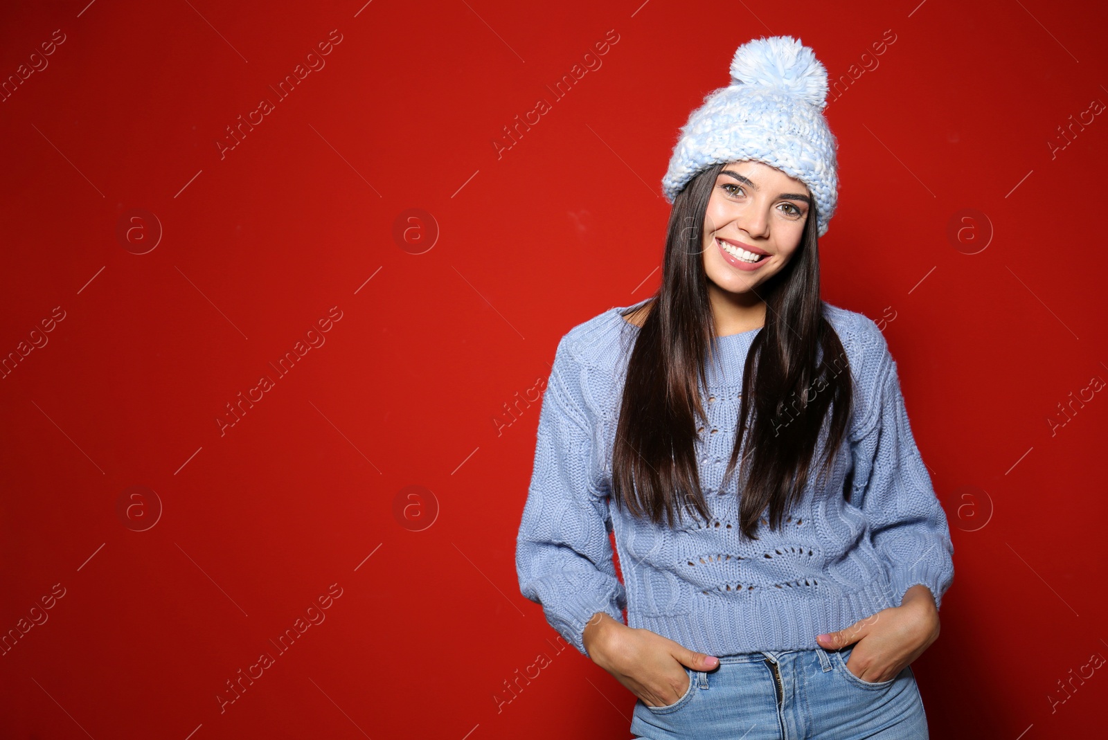 Photo of Young woman in warm sweater with hat on red background. Space for text