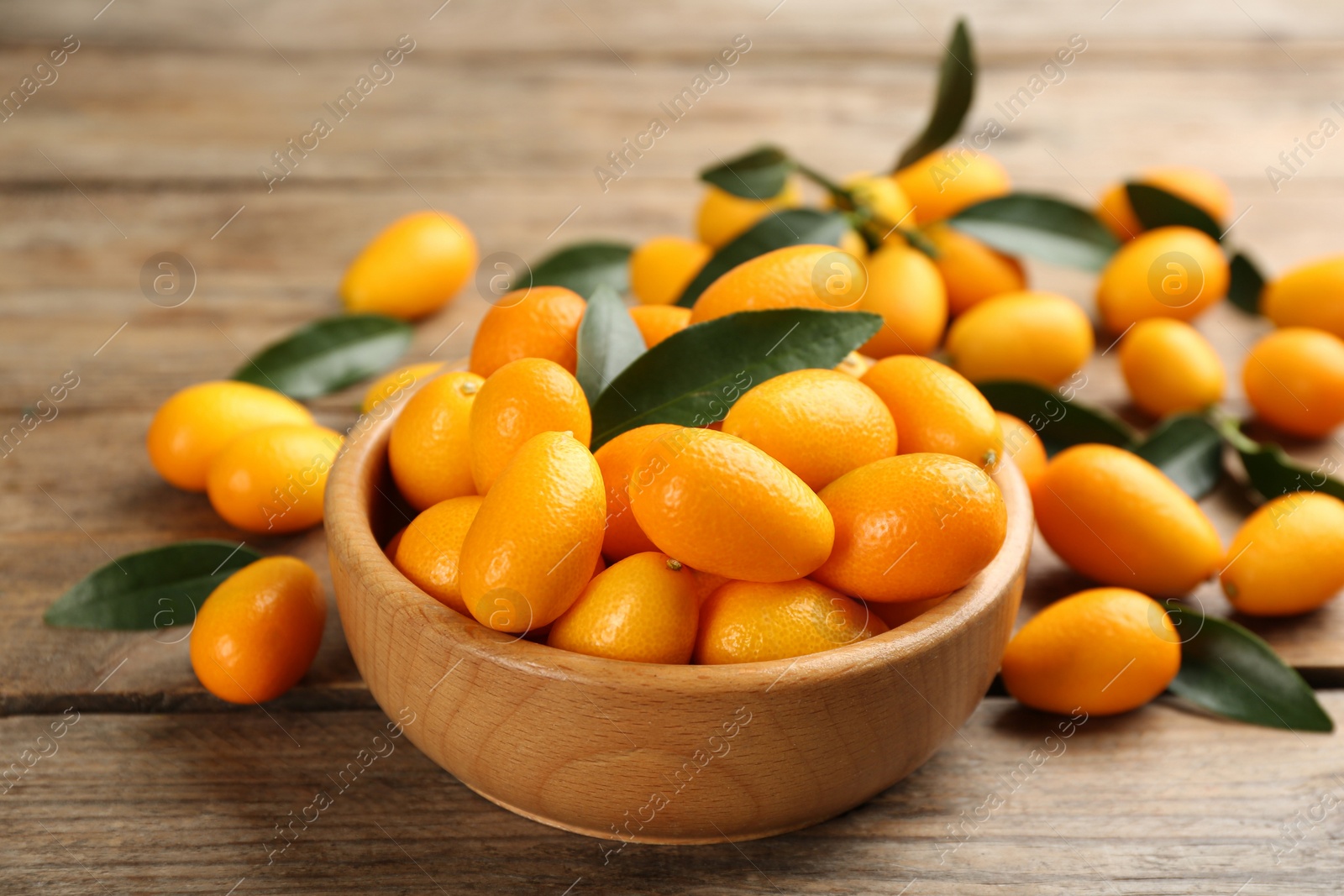 Photo of Fresh ripe kumquats in bowl on wooden table