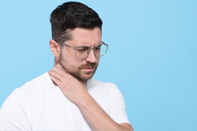 Man suffering from sore throat on light blue background, space for text