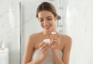 Photo of Young woman with face cream in bathroom