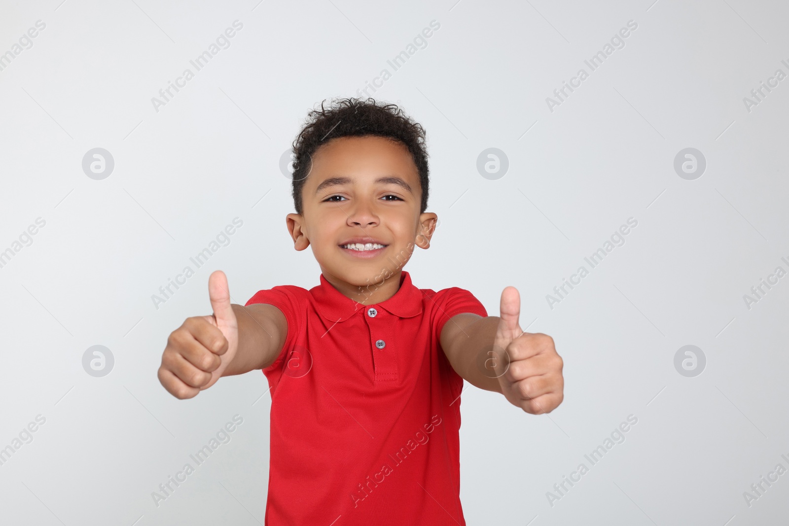 Photo of African-American boy showing thumbs up on light grey background